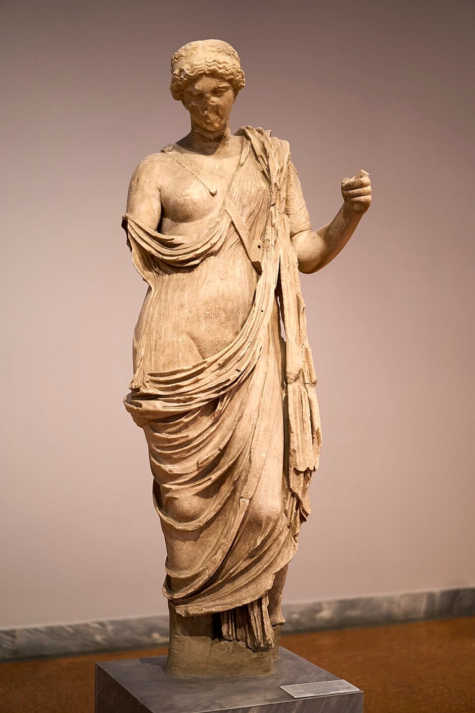 A statue of Aphrodite Areia, Warlike Aphrodite, in aged yellowed marble. She is missing an arm, and is wearing a draped cloth around Her body.
